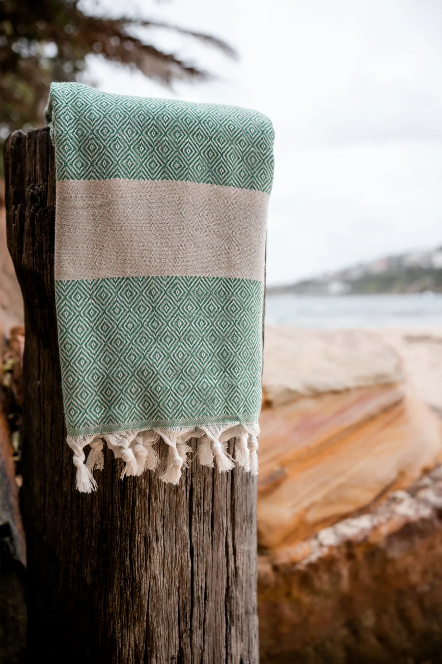 Green diamond-weave fouta folded on a wooden post beside the coast