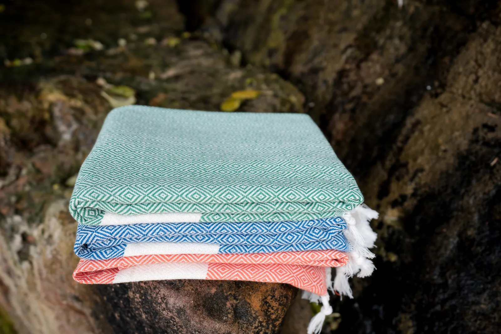 Stack of colourful diamond-weave foutas on coastal rocks