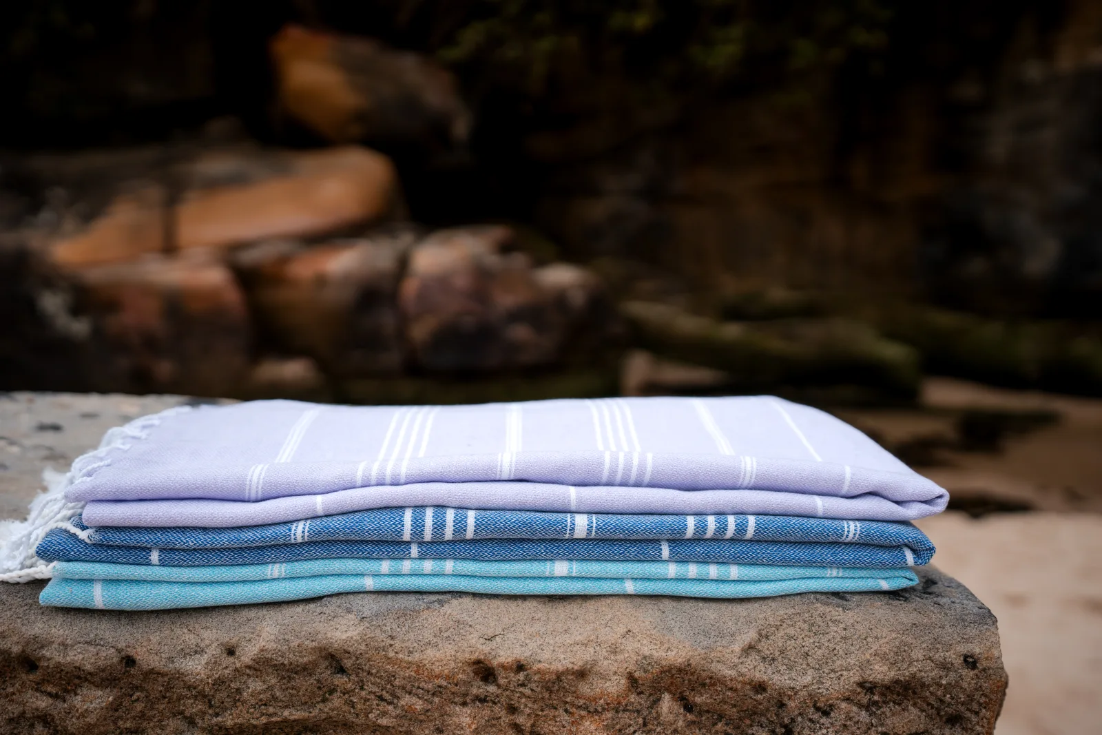 Folded blue and lavender foutas stacked on coastal rock